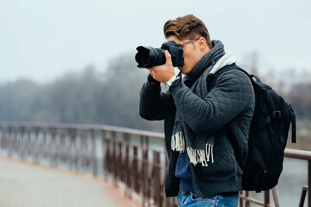 Photographer with a backpack shooting outdoors on a misty riverside promenade